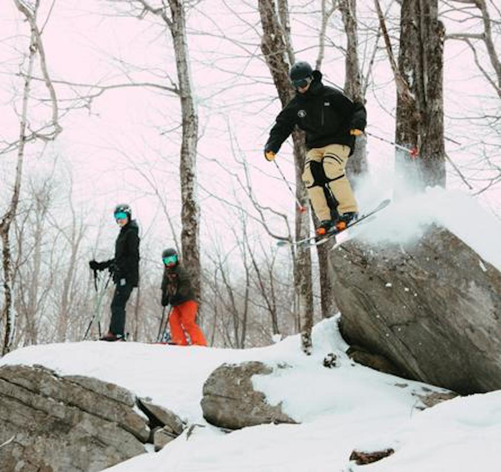 skier jumping off a rock in the woods at bromley mountain
